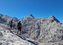 Two hikers ascending rocky terrain in an impressive mountainous landscape with steep peaks.