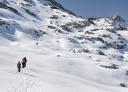 People walking along a snow-covered path in a mountainous winter landscape.