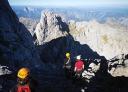 A group of hikers walk along a rocky path under imposing mountain formations.