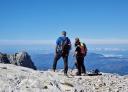 Three mountaineers stand on a rocky summit overlooking the landscape.