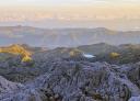 Aerial views of a rocky mountain landscape with peaks and a lake in the distance.