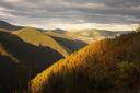 Mountain valleys tinged with orange and yellow at sunset, under a cloudy sky.