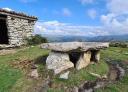An ancient stone dolmen stands imposingly in a green mountain landscape.