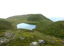 Un sereno lago de montaña rodeado de picos verdes bajo un cielo despejado