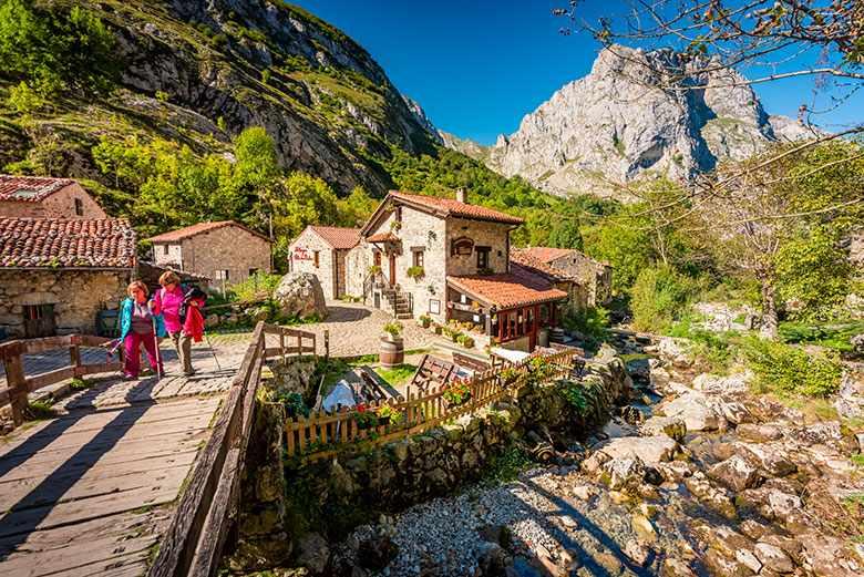 Photo of two people crossing the wooden bridge in the village of Bulnes, in the council of Cabrales.