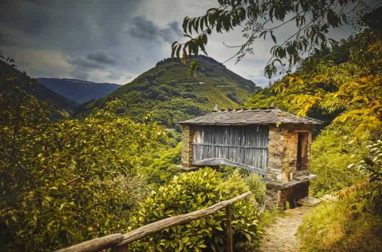 Cabazo traditionnel en pierre et en bois dans les environs du musée ethnographique d'Esquíos, à Taramundi, entouré d'une végétation dense et de collines couvertes de forêts.