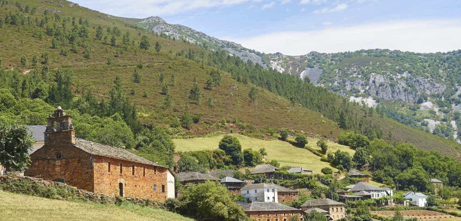 Immagine del villaggio di Seroiro, con la chiesa in primo piano in pietra e il tetto in ardesia, come il resto delle case alle sue spalle. Il villaggio è circondato da pendii montuosi. Colori variegati tra il verde chiaro di alcuni prati e il verde scuro di alberi e cespugli, alcuni dei quali sfiorano il marrone autunnale. Sullo sfondo una montagna più alta con alcune rocce.