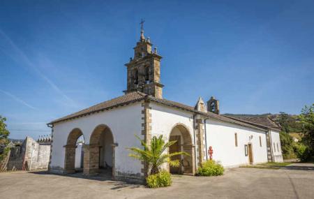 La iglesia está situada en primer plano, en una la plaza amplia. El diseño es sencillo, piedra en las esquinas y fachadas revocadas en blanco. En la fachada principal, dos arcos y uno en la lateral con dos macetas de palmeras. Coronan el edificio dos torres campanario, sobre cubierta de teja roja.  El cielo azul,  está dibujado con estelas de nubes blancas.