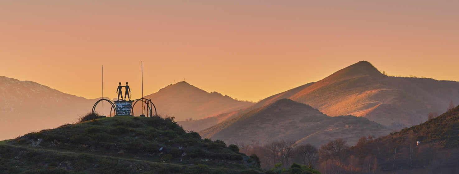Schöner Blick auf den Sonnenuntergang vom Bergarbeiterdenkmal aus. Eine Bronzeskulptur auf einem Hügel, zwei Bergleute auf einem Sockel und im Hintergrund ragen einige Berge steil in den orangefarbenen Himmel.