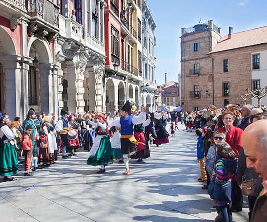 Un grupo de personas baila con el traje regional de Asturias en el centro de la calle, mientras el público forma un pasillo a ambos lados en Avilés.