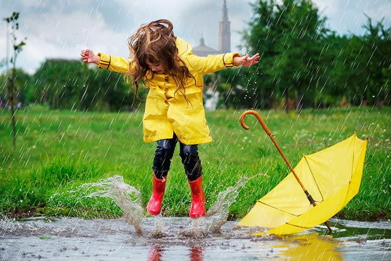 Niña con chubasquero amarillo saltando en un charco bajo la lluvia