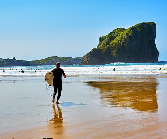 Surfista en la playa de San Martín en el concejo de Llanes con la gran roca característica de esta playa al fondo.