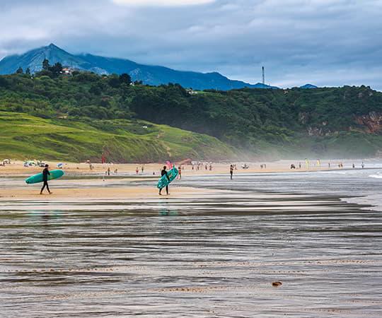 Surfistas en la playa de La Vega en Ribadesella con las montañas al fondo.