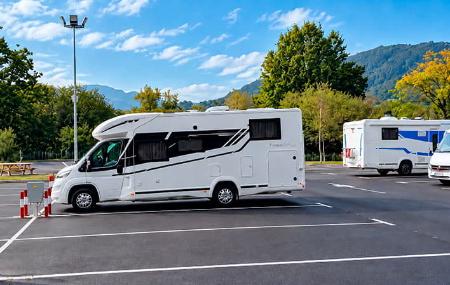 Autocaravana estacionada en una de las plazas del área de Lugones, con otras autocaravanas y vegetación alrededor.