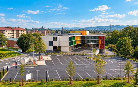Vista elevada del área de autocaravanas de Lugones, con sus plazas de aparcamiento y un edificio moderno al fondo.