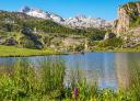 Lago Ercina con los Picos de Europa al fondo, rodeado de praderas y vegetación de montaña.