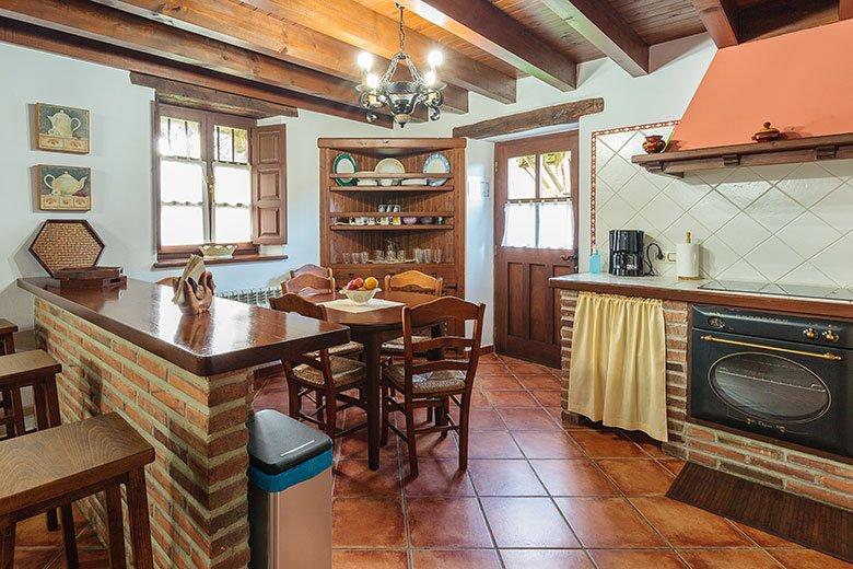 Foto de la cocina con una barra en primer plano y fogones con chimenea.  Casa rural La Venta Los Probes (de la marca Aldeas de Asturias) situada en el concejo de Llanes.