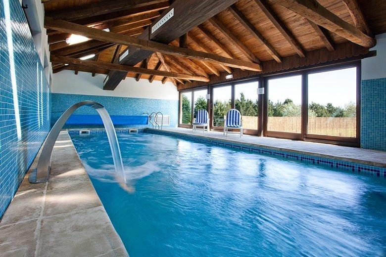 Piscina interior climatizada con grandes ventanales y estructura de madera
