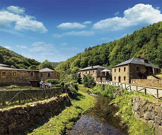 The village of Pumares, where a river can be seen between the houses and a family is eating in the meadow of one of them. Council of Santa Eulalia de Oscos.
