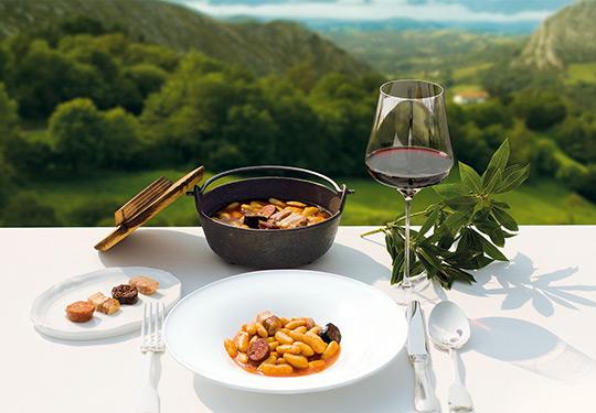 Photo of a plate of fabada with a landscape in the background.